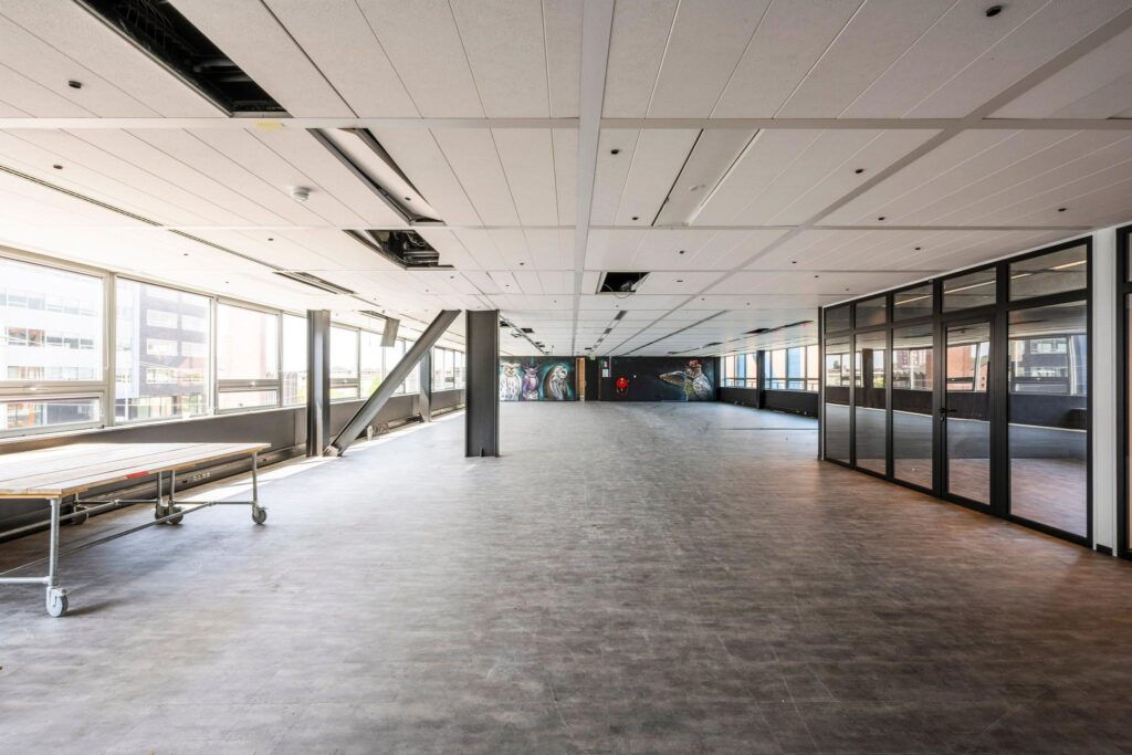 Spacious, empty office space at Bos en Lommerplein with large windows and wall art.